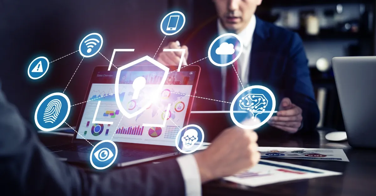 Two men in a business meeting, looking at a laptop screen with cybersecurity-related icons.