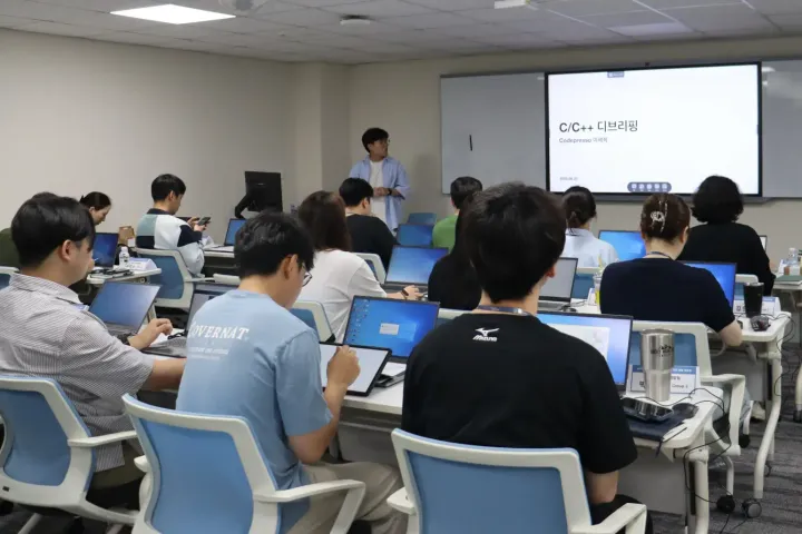 Devtalk 디브리핑 현장에서 연사님이 진단 결과에 대해 설명하는 모습과 참여자 현대오토에버 직원들의 뒷모습